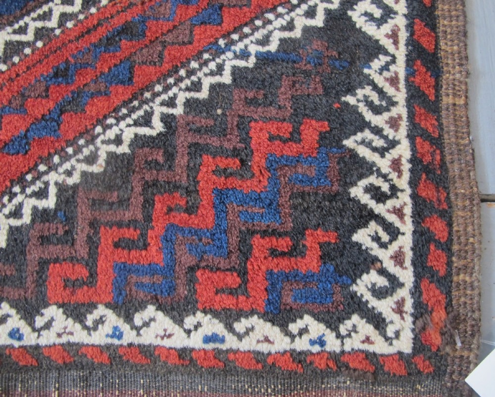 An antique hand-woven Belouch wool rug featuring geometric octagonal medallions in deep red, navy blue, and dark brown tones. View VI