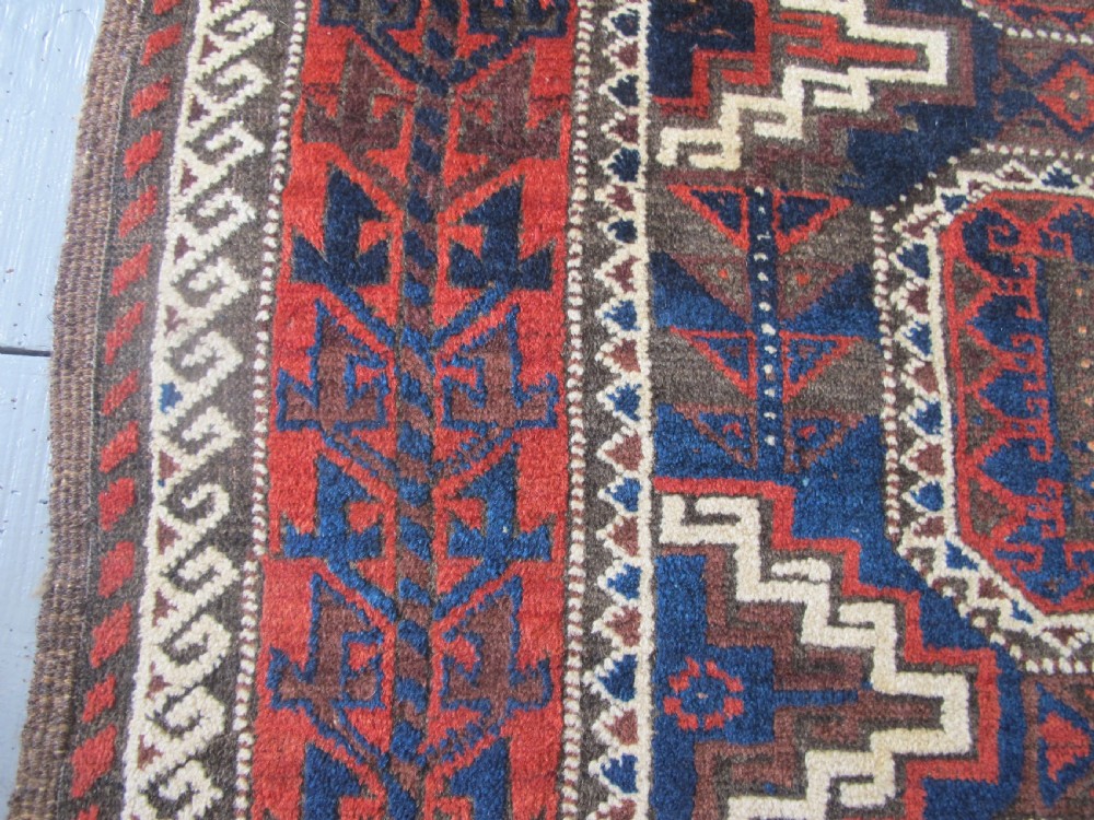 An antique hand-woven Belouch wool rug featuring geometric octagonal medallions in deep red, navy blue, and dark brown tones. View VII