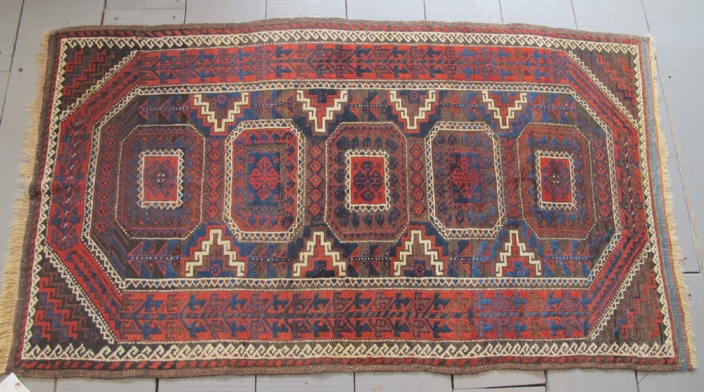 An antique hand-woven Belouch wool rug featuring geometric octagonal medallions in deep red, navy blue, and dark brown tones. View VIII