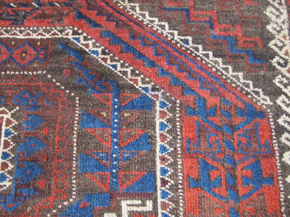 An antique hand-woven Belouch wool rug featuring geometric octagonal medallions in deep red, navy blue, and dark brown tones. View IX