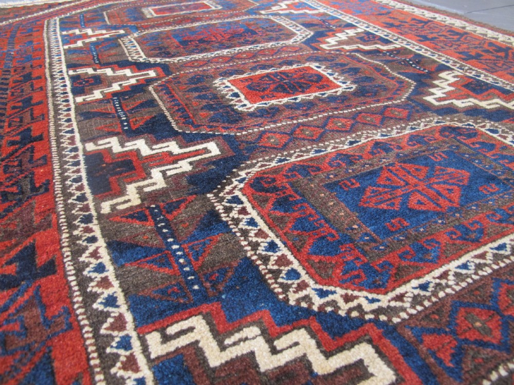An antique hand-woven Belouch wool rug featuring geometric octagonal medallions in deep red, navy blue, and dark brown tones. View X