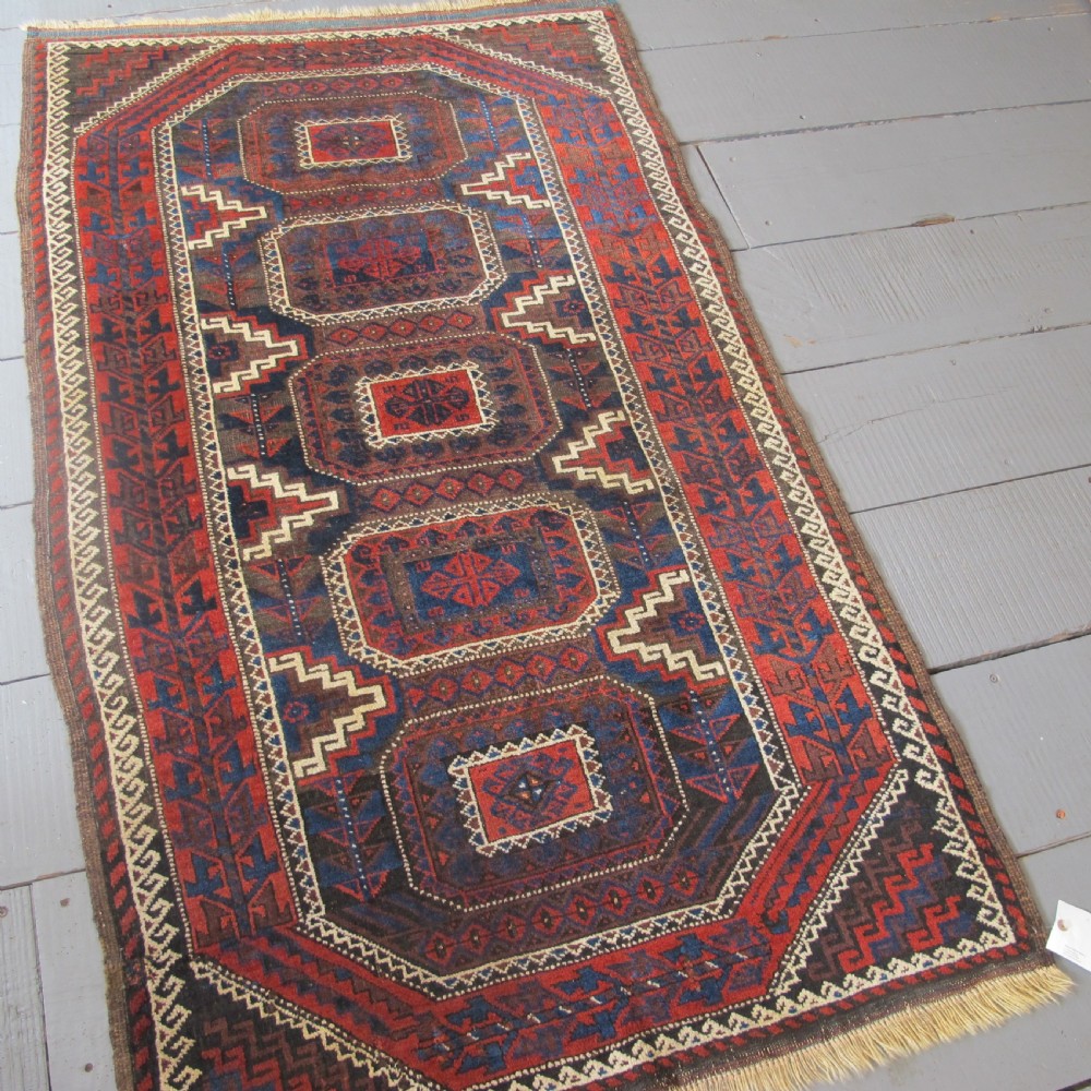 An antique hand-woven Belouch wool rug featuring geometric octagonal medallions in deep red, navy blue, and dark brown tones. View XI