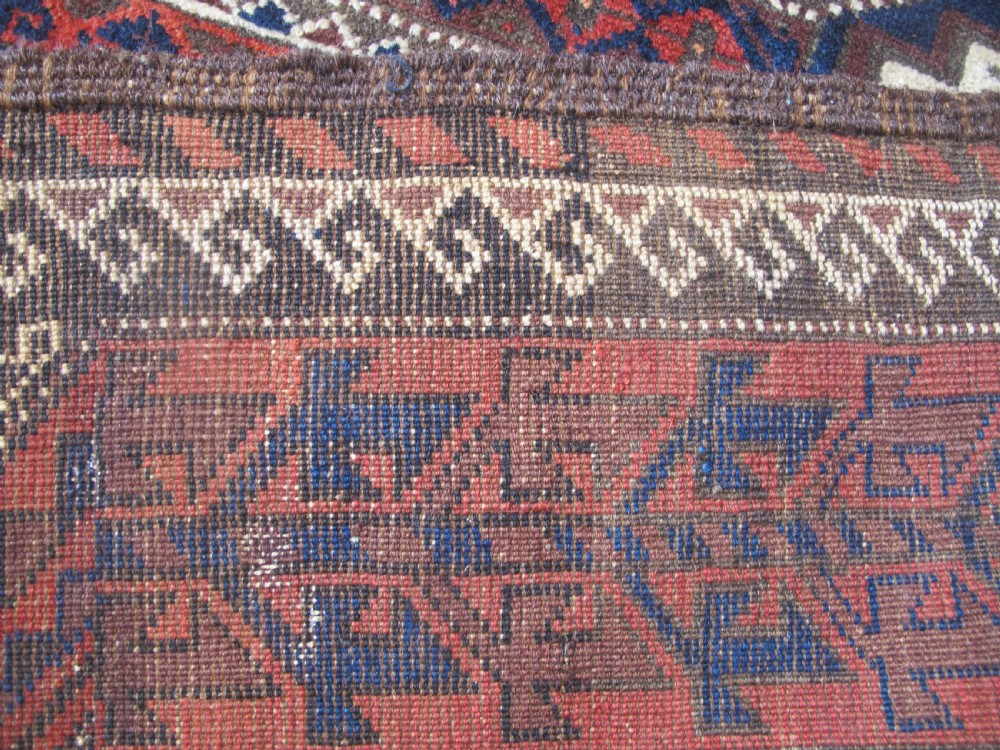 An antique hand-woven Belouch wool rug featuring geometric octagonal medallions in deep red, navy blue, and dark brown tones. View XII