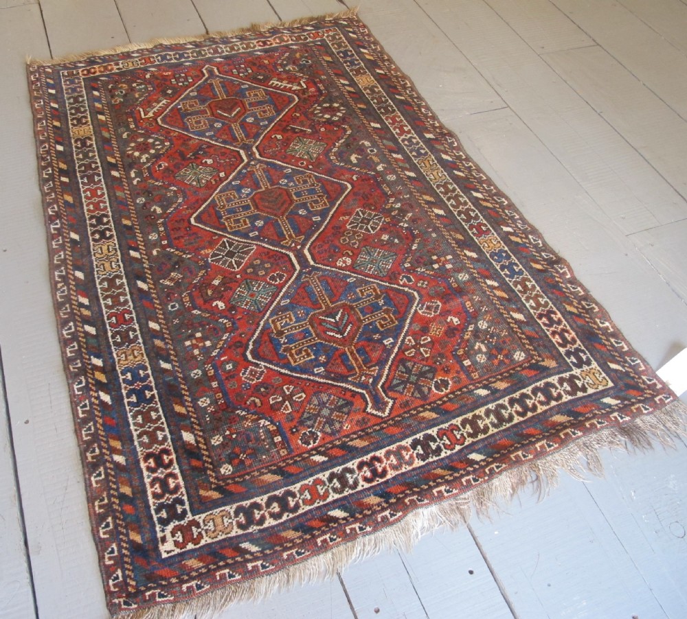 A hand-knotted antique Persian Shiraz wool rug featuring three geometric diamond medallions in blue and cream on a deep terracotta red field with decorative tribal borders.