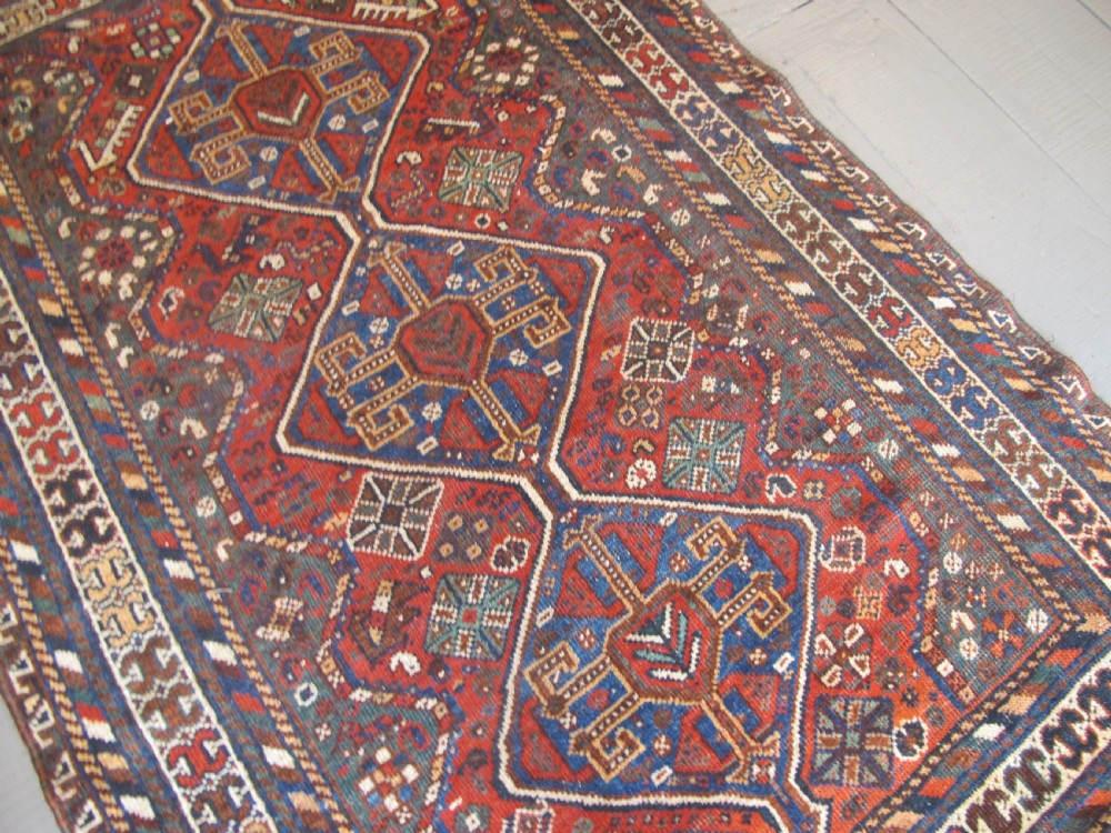 A hand-knotted antique Persian Shiraz wool rug featuring three geometric diamond medallions in blue and cream on a deep terracotta red field with decorative tribal borders. View II