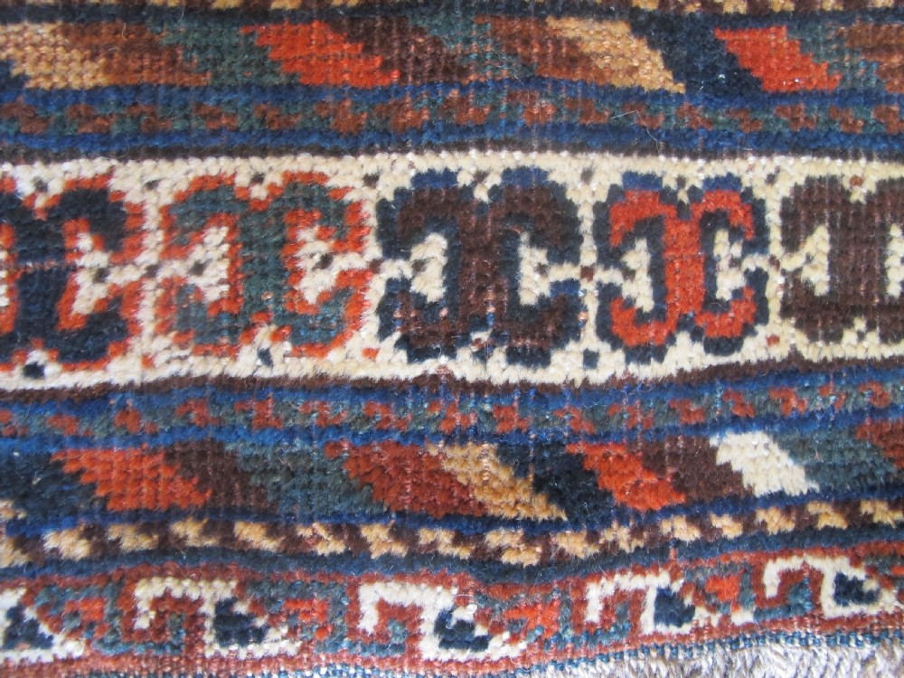 A hand-knotted antique Persian Shiraz wool rug featuring three geometric diamond medallions in blue and cream on a deep terracotta red field with decorative tribal borders. View IV