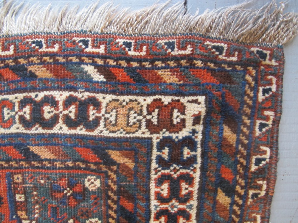 A hand-knotted antique Persian Shiraz wool rug featuring three geometric diamond medallions in blue and cream on a deep terracotta red field with decorative tribal borders. View V