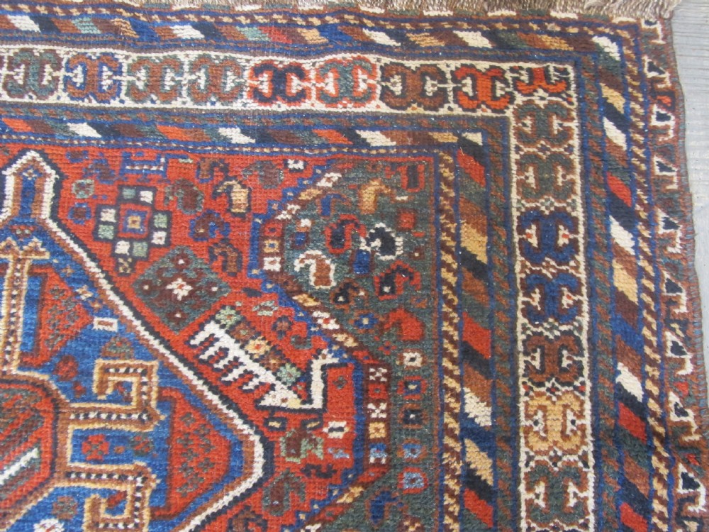 A hand-knotted antique Persian Shiraz wool rug featuring three geometric diamond medallions in blue and cream on a deep terracotta red field with decorative tribal borders. View VIII