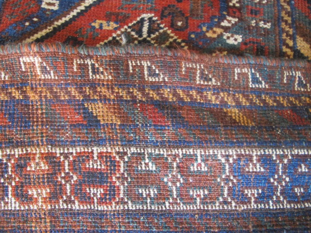 A hand-knotted antique Persian Shiraz wool rug featuring three geometric diamond medallions in blue and cream on a deep terracotta red field with decorative tribal borders. View X