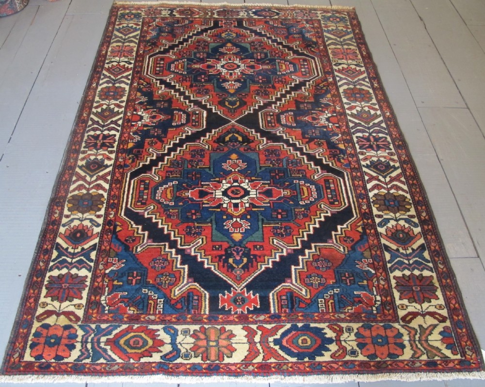 An antique late 19th-century Persian village rug featuring a double geometric medallion in red and navy blue surrounded by a cream floral border.