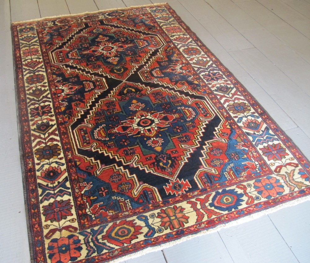 An antique late 19th-century Persian village rug featuring a double geometric medallion in red and navy blue surrounded by a cream floral border. View II