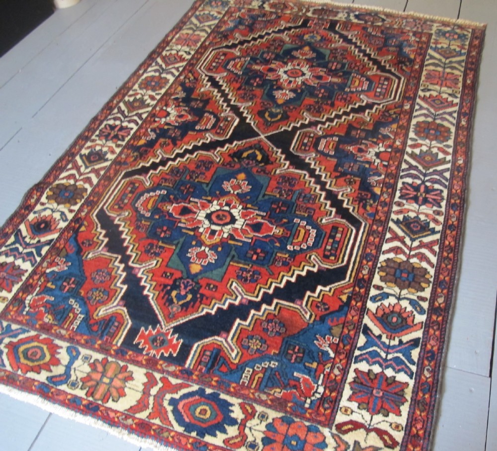 An antique late 19th-century Persian village rug featuring a double geometric medallion in red and navy blue surrounded by a cream floral border. View III