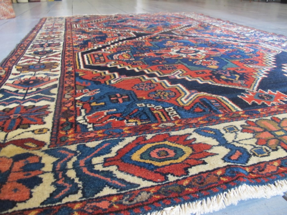 An antique late 19th-century Persian village rug featuring a double geometric medallion in red and navy blue surrounded by a cream floral border. View IV