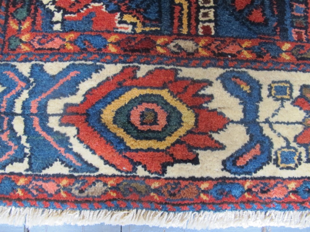 An antique late 19th-century Persian village rug featuring a double geometric medallion in red and navy blue surrounded by a cream floral border. View V