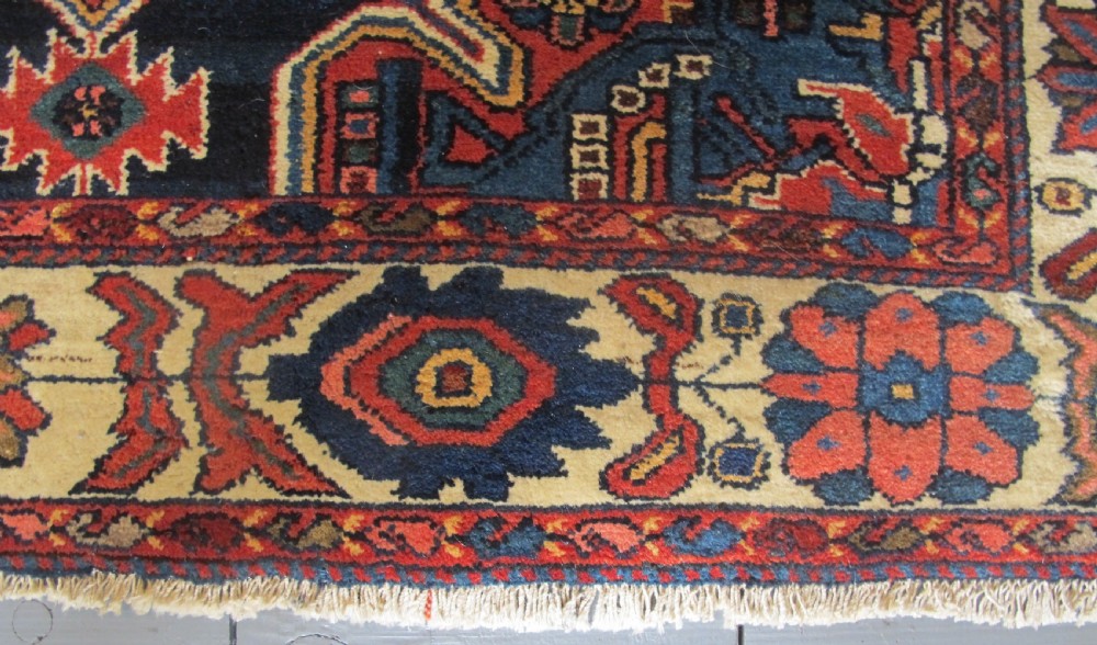 An antique late 19th-century Persian village rug featuring a double geometric medallion in red and navy blue surrounded by a cream floral border. View VI