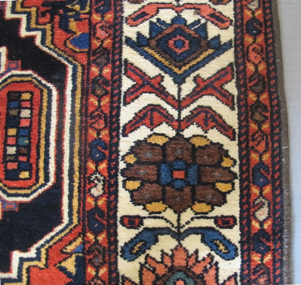 An antique late 19th-century Persian village rug featuring a double geometric medallion in red and navy blue surrounded by a cream floral border. View VII