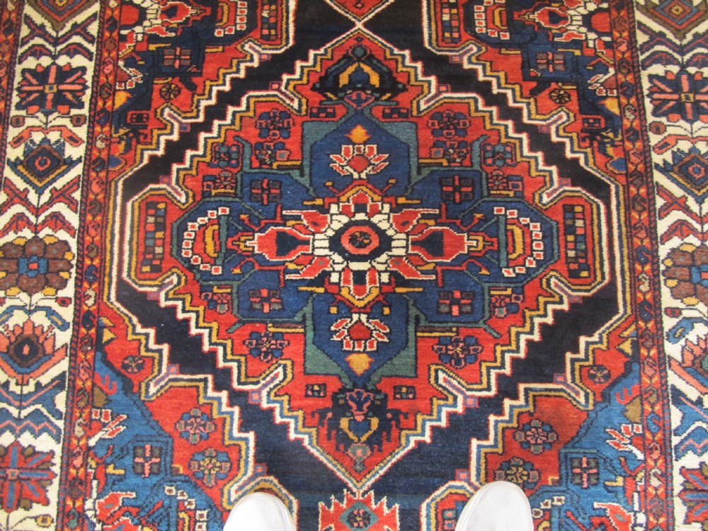 An antique late 19th-century Persian village rug featuring a double geometric medallion in red and navy blue surrounded by a cream floral border. View VIII