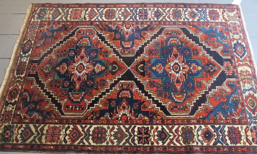 An antique late 19th-century Persian village rug featuring a double geometric medallion in red and navy blue surrounded by a cream floral border. View IX