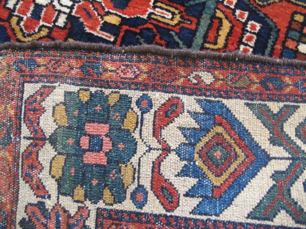 An antique late 19th-century Persian village rug featuring a double geometric medallion in red and navy blue surrounded by a cream floral border. View X
