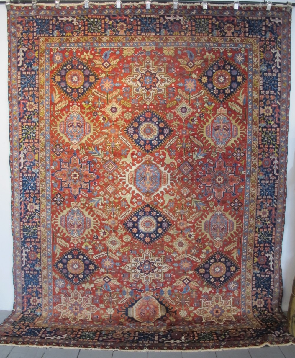 An antique late 19th-century Persian Karaja wool carpet featuring a terracotta red field filled with geometric medallions and surrounded by a detailed dark indigo border.