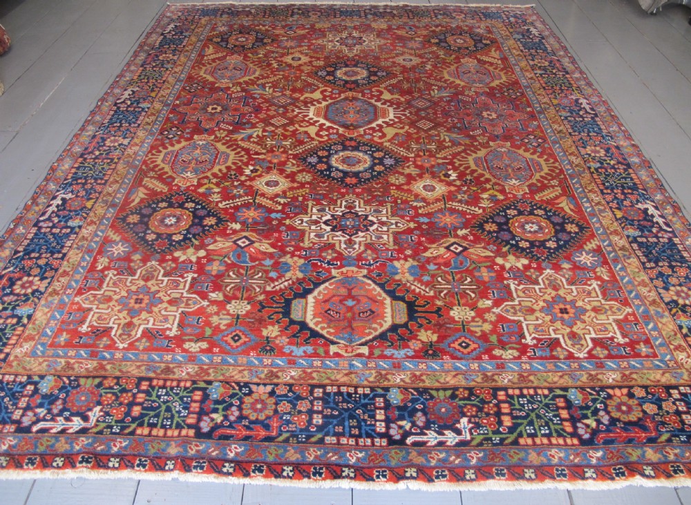 An antique late 19th-century Persian Karaja wool carpet featuring a terracotta red field filled with geometric medallions and surrounded by a detailed dark indigo border. View II