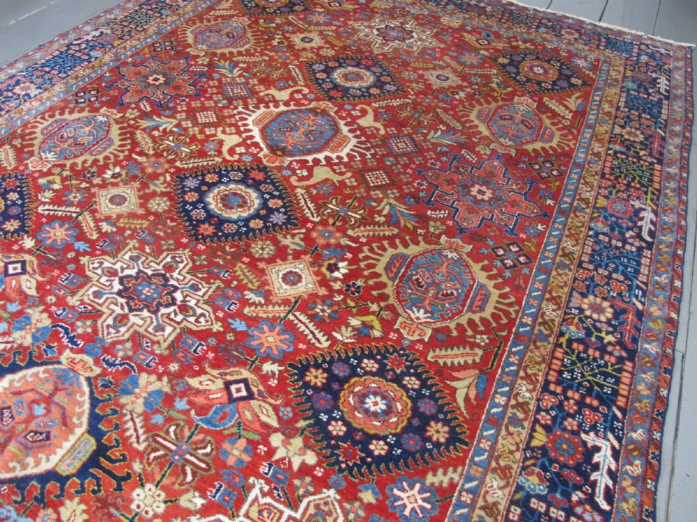 An antique late 19th-century Persian Karaja wool carpet featuring a terracotta red field filled with geometric medallions and surrounded by a detailed dark indigo border. View IV