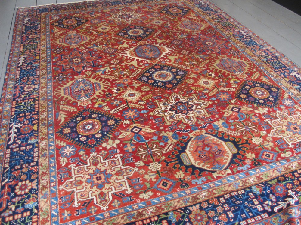 An antique late 19th-century Persian Karaja wool carpet featuring a terracotta red field filled with geometric medallions and surrounded by a detailed dark indigo border. View V