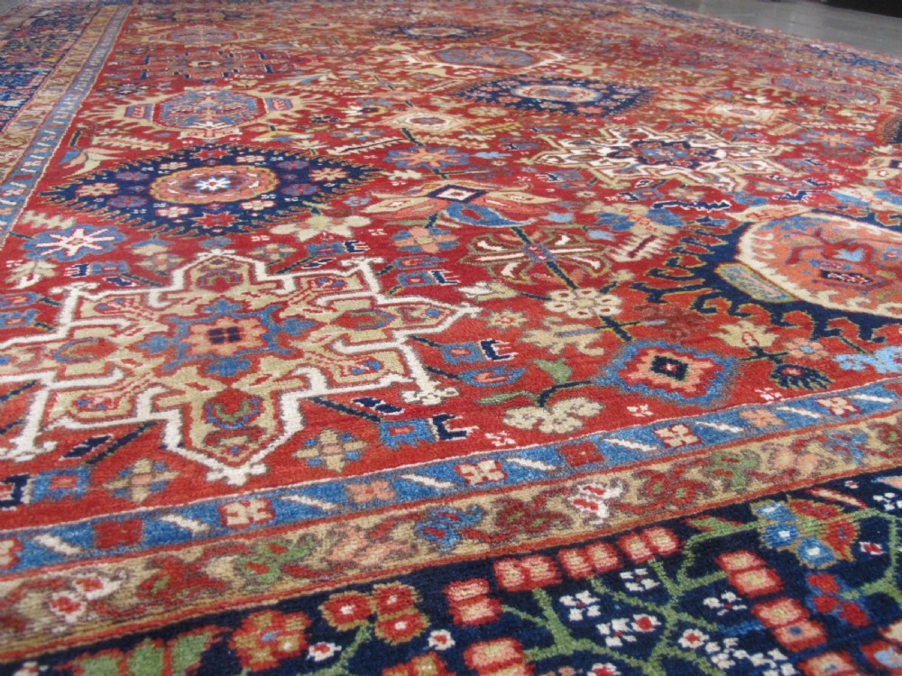 An antique late 19th-century Persian Karaja wool carpet featuring a terracotta red field filled with geometric medallions and surrounded by a detailed dark indigo border. View VI