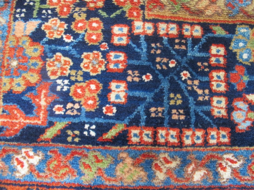 An antique late 19th-century Persian Karaja wool carpet featuring a terracotta red field filled with geometric medallions and surrounded by a detailed dark indigo border. View VII