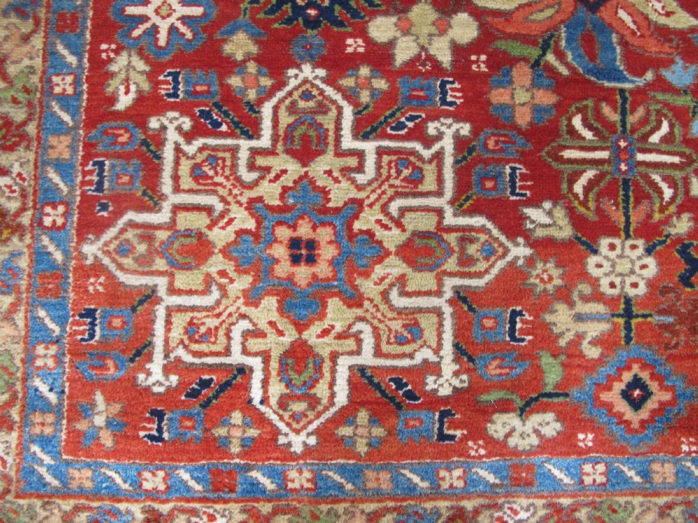 An antique late 19th-century Persian Karaja wool carpet featuring a terracotta red field filled with geometric medallions and surrounded by a detailed dark indigo border. View X