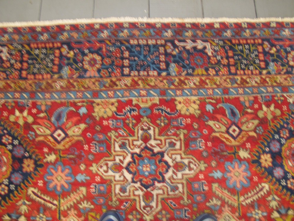 An antique late 19th-century Persian Karaja wool carpet featuring a terracotta red field filled with geometric medallions and surrounded by a detailed dark indigo border. View XII