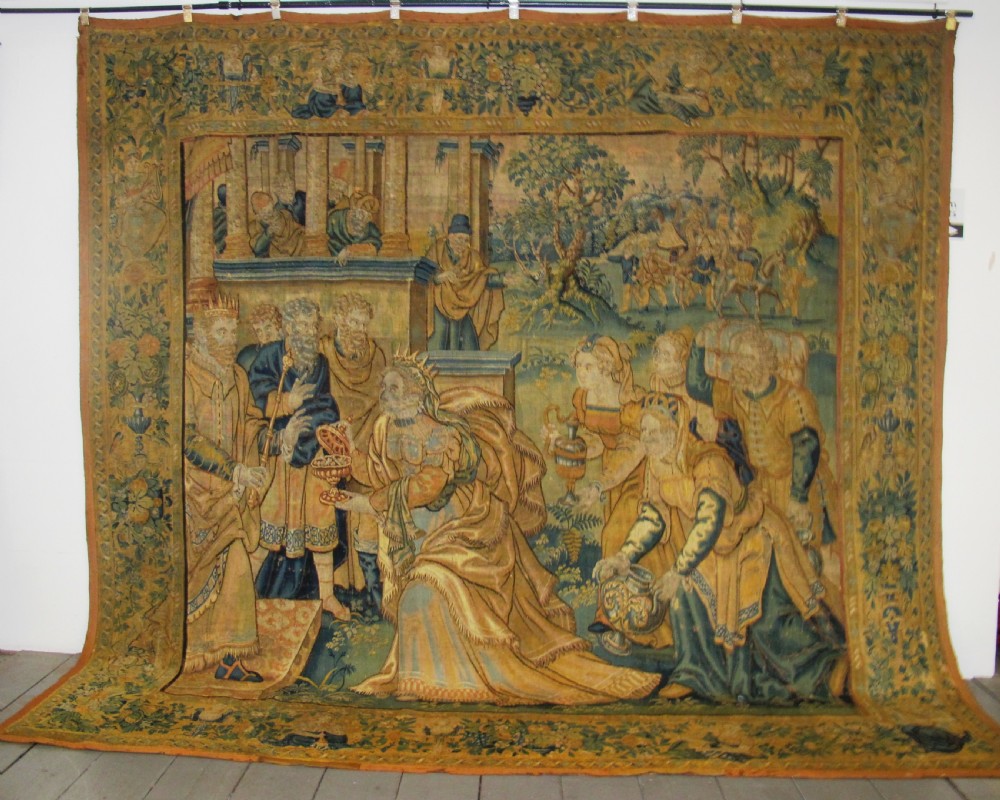A large 16th-century Flemish Renaissance tapestry woven with figures in classical attire framed by an elaborate floral and fruit border.