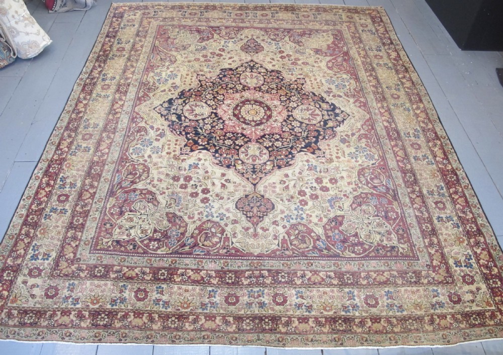 A large 19th-century Kirman Laver hand-knotted wool carpet featuring a central starburst floral medallion on an ivory ground surrounded by multi-banded floral borders in shades of crimson and navy blue.