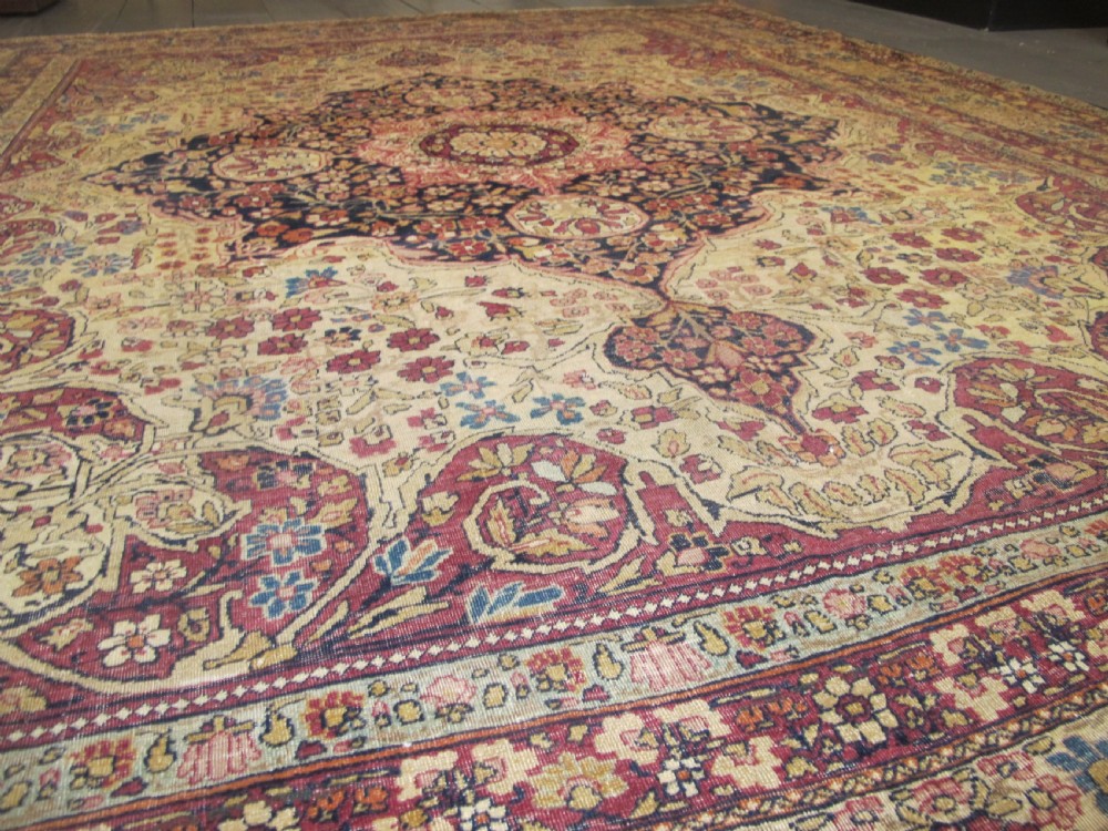 A large 19th-century Kirman Laver hand-knotted wool carpet featuring a central starburst floral medallion on an ivory ground surrounded by multi-banded floral borders in shades of crimson and navy blue. View II