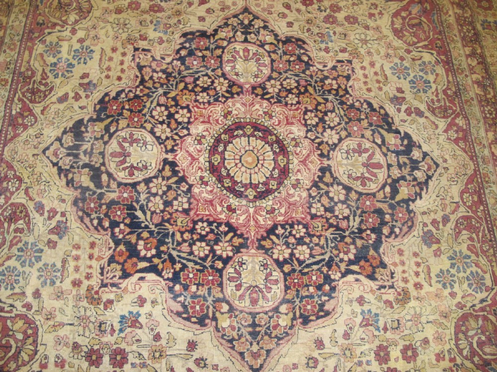 A large 19th-century Kirman Laver hand-knotted wool carpet featuring a central starburst floral medallion on an ivory ground surrounded by multi-banded floral borders in shades of crimson and navy blue. View III