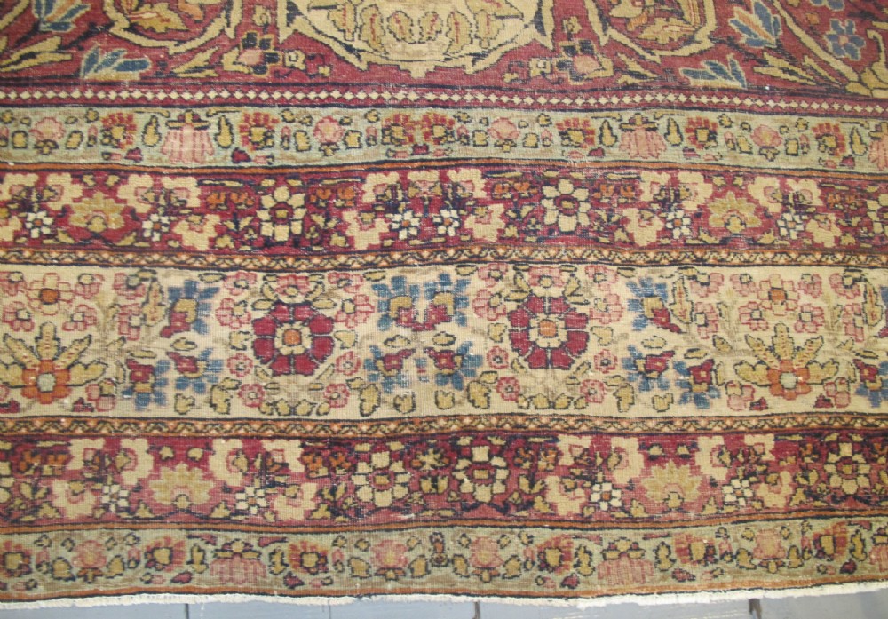 A large 19th-century Kirman Laver hand-knotted wool carpet featuring a central starburst floral medallion on an ivory ground surrounded by multi-banded floral borders in shades of crimson and navy blue. View V