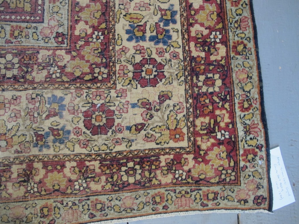 A large 19th-century Kirman Laver hand-knotted wool carpet featuring a central starburst floral medallion on an ivory ground surrounded by multi-banded floral borders in shades of crimson and navy blue. View VI