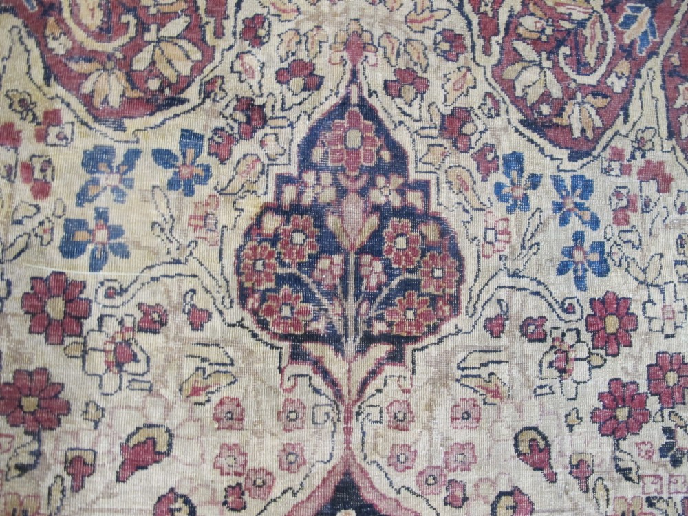 A large 19th-century Kirman Laver hand-knotted wool carpet featuring a central starburst floral medallion on an ivory ground surrounded by multi-banded floral borders in shades of crimson and navy blue. View VII