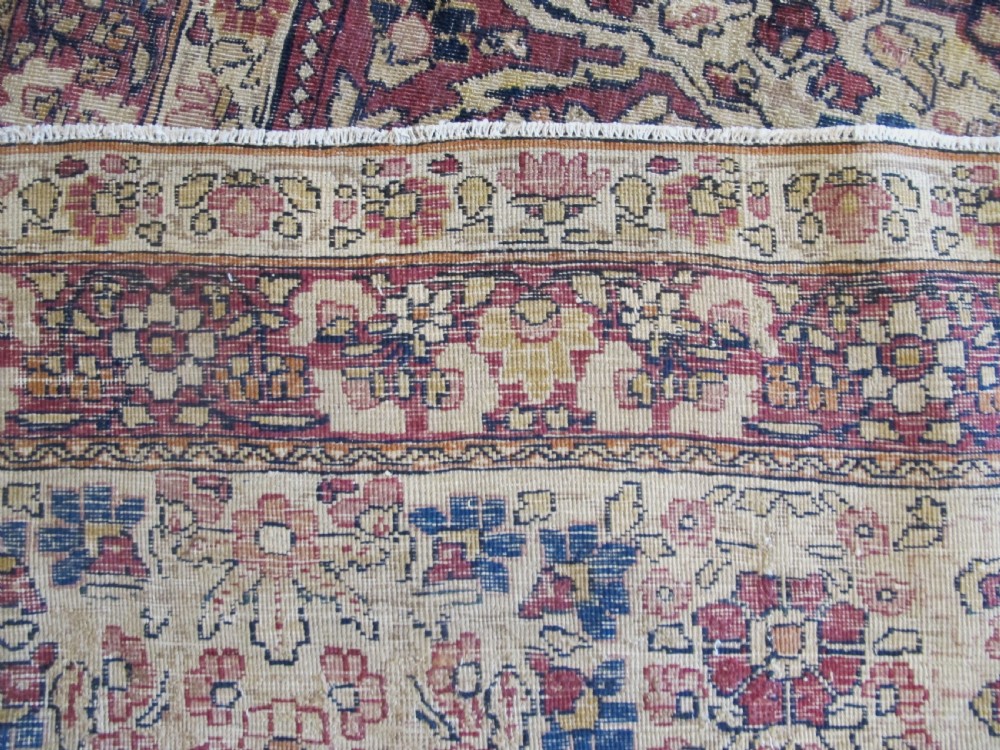 A large 19th-century Kirman Laver hand-knotted wool carpet featuring a central starburst floral medallion on an ivory ground surrounded by multi-banded floral borders in shades of crimson and navy blue. View IX