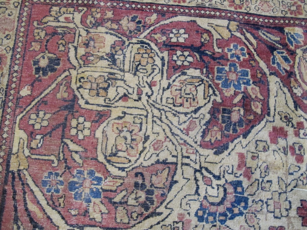 A large 19th-century Kirman Laver hand-knotted wool carpet featuring a central starburst floral medallion on an ivory ground surrounded by multi-banded floral borders in shades of crimson and navy blue. View X