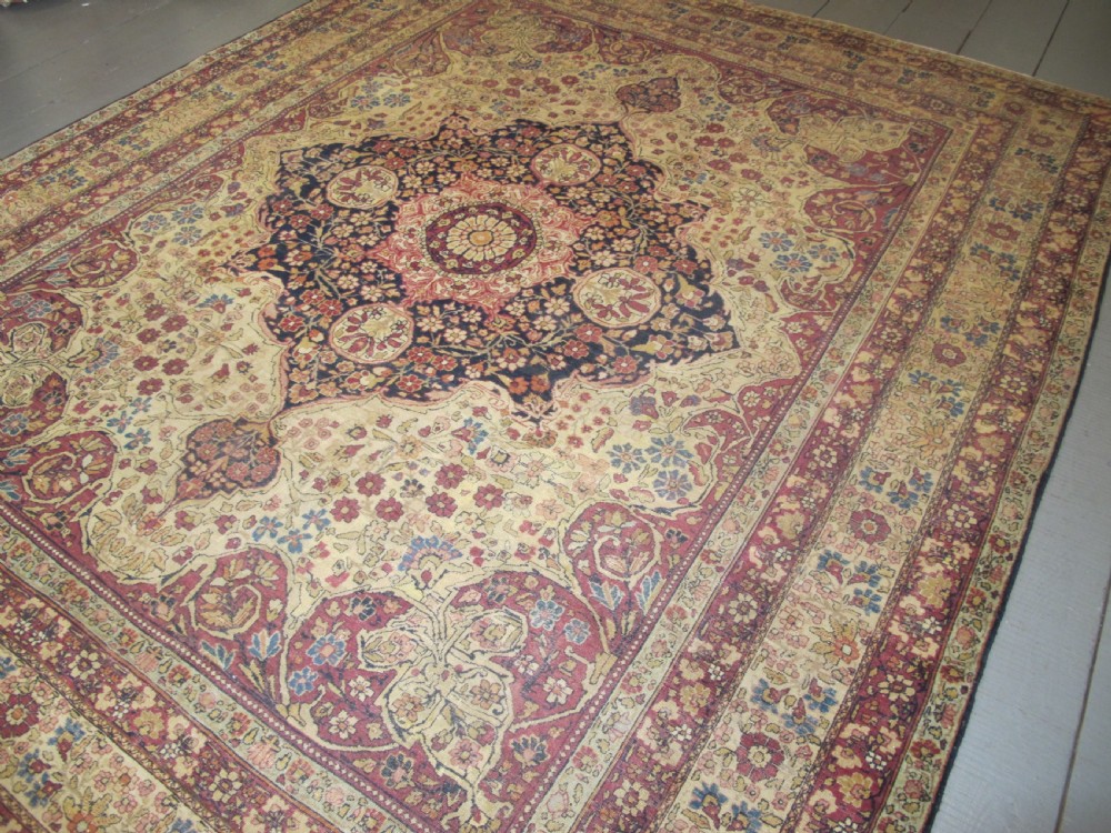 A large 19th-century Kirman Laver hand-knotted wool carpet featuring a central starburst floral medallion on an ivory ground surrounded by multi-banded floral borders in shades of crimson and navy blue. View XI