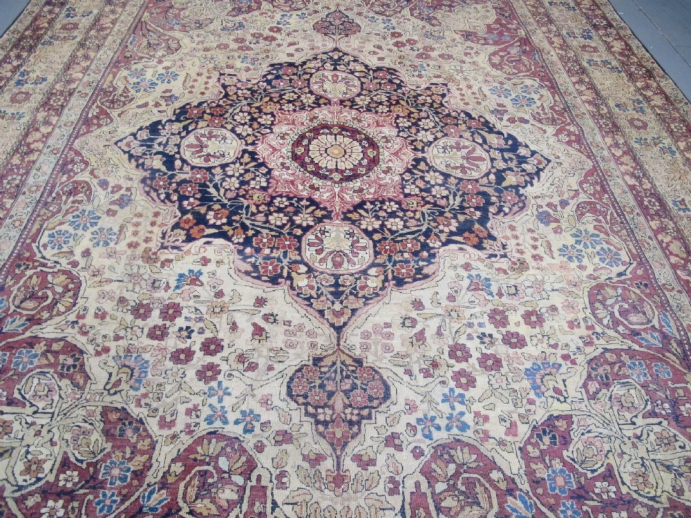 A large 19th-century Kirman Laver hand-knotted wool carpet featuring a central starburst floral medallion on an ivory ground surrounded by multi-banded floral borders in shades of crimson and navy blue. View XII