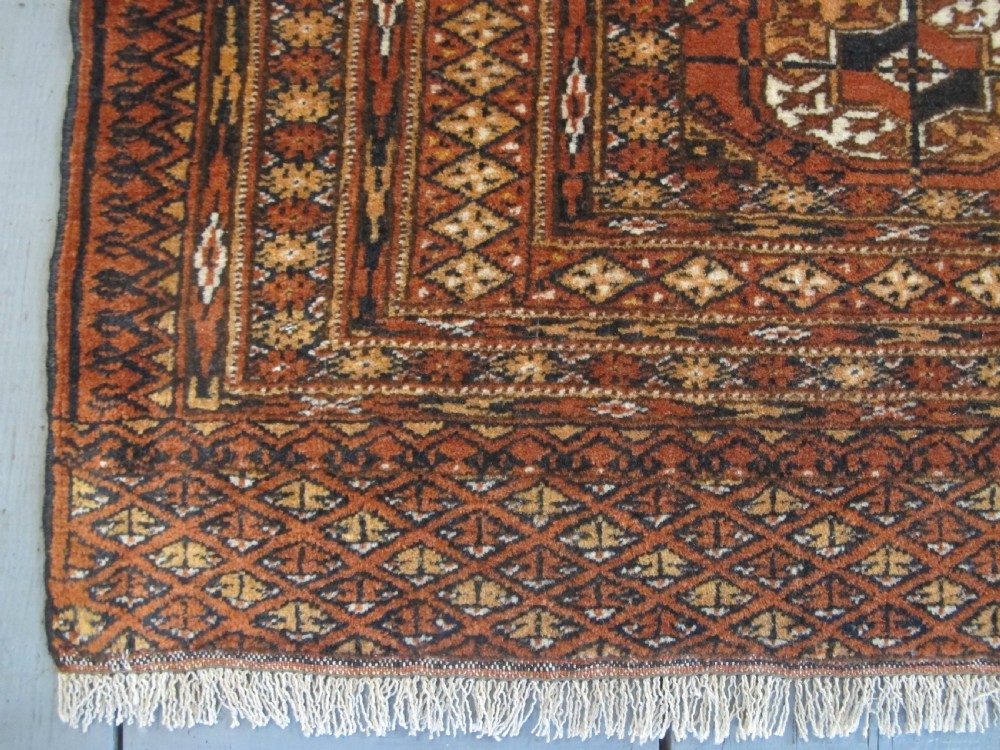 A rectangular hand-knotted Tekke rug featuring repeating octagonal gul motifs in dark blue and ivory across a terracotta red wool ground. View II