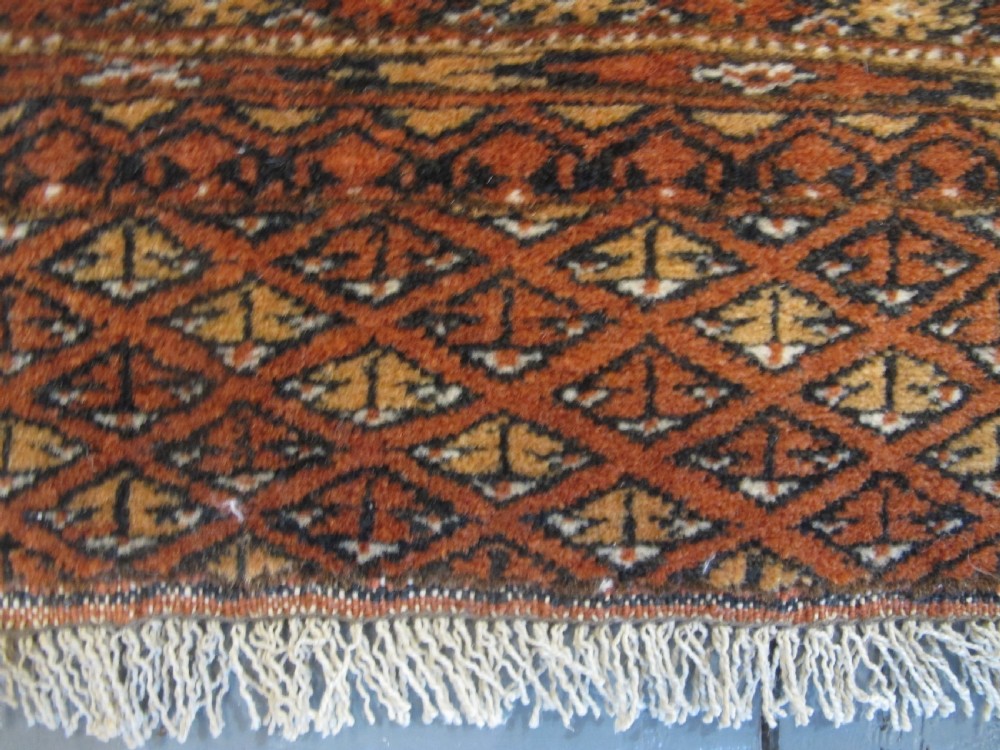 A rectangular hand-knotted Tekke rug featuring repeating octagonal gul motifs in dark blue and ivory across a terracotta red wool ground. View VI