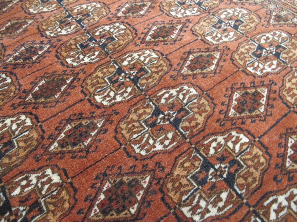 A rectangular hand-knotted Tekke rug featuring repeating octagonal gul motifs in dark blue and ivory across a terracotta red wool ground. View VIII
