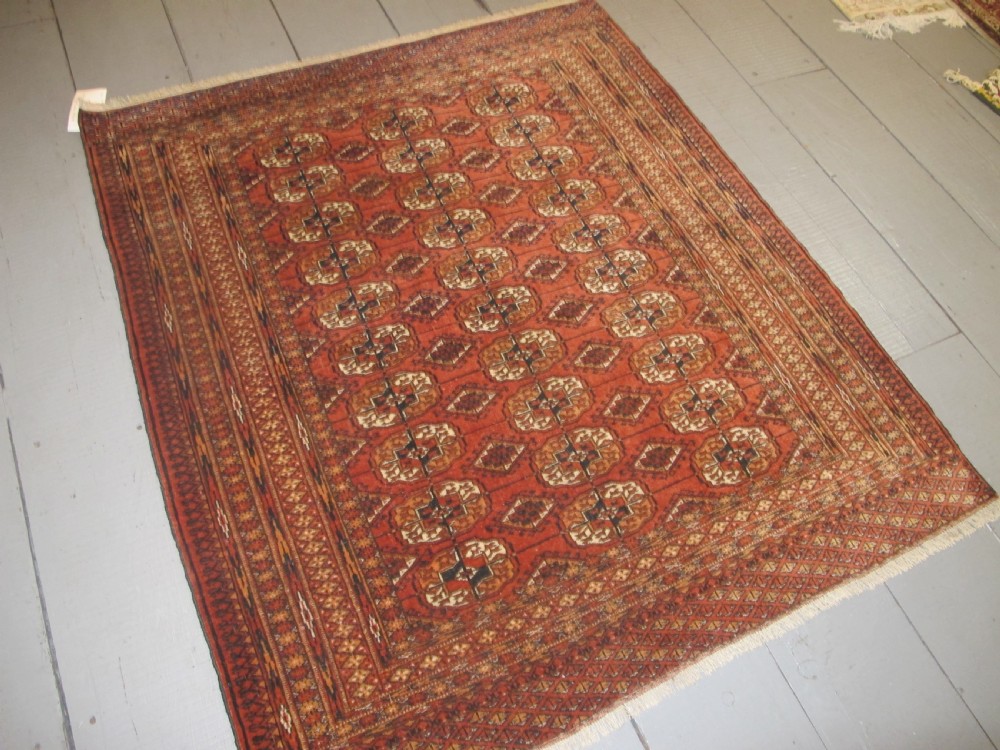 A rectangular hand-knotted Tekke rug featuring repeating octagonal gul motifs in dark blue and ivory across a terracotta red wool ground. View IX