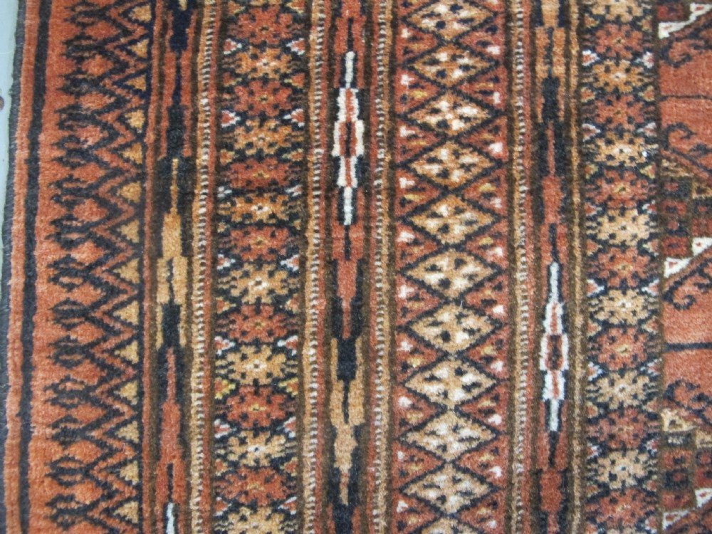 A rectangular hand-knotted Tekke rug featuring repeating octagonal gul motifs in dark blue and ivory across a terracotta red wool ground. View XI