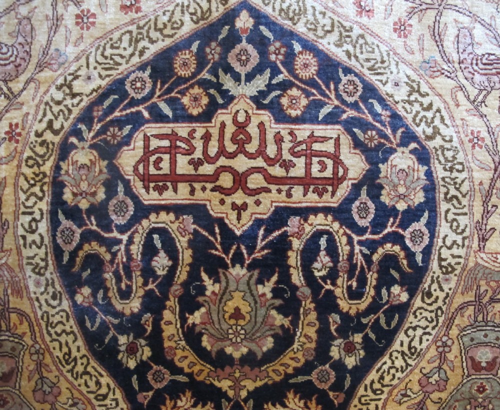 A mid-20th-century Turkish silk rug featuring a dark navy mihrab arch filled with floral motifs, surrounded by an ochre border with calligraphic script and bird illustrations. View V