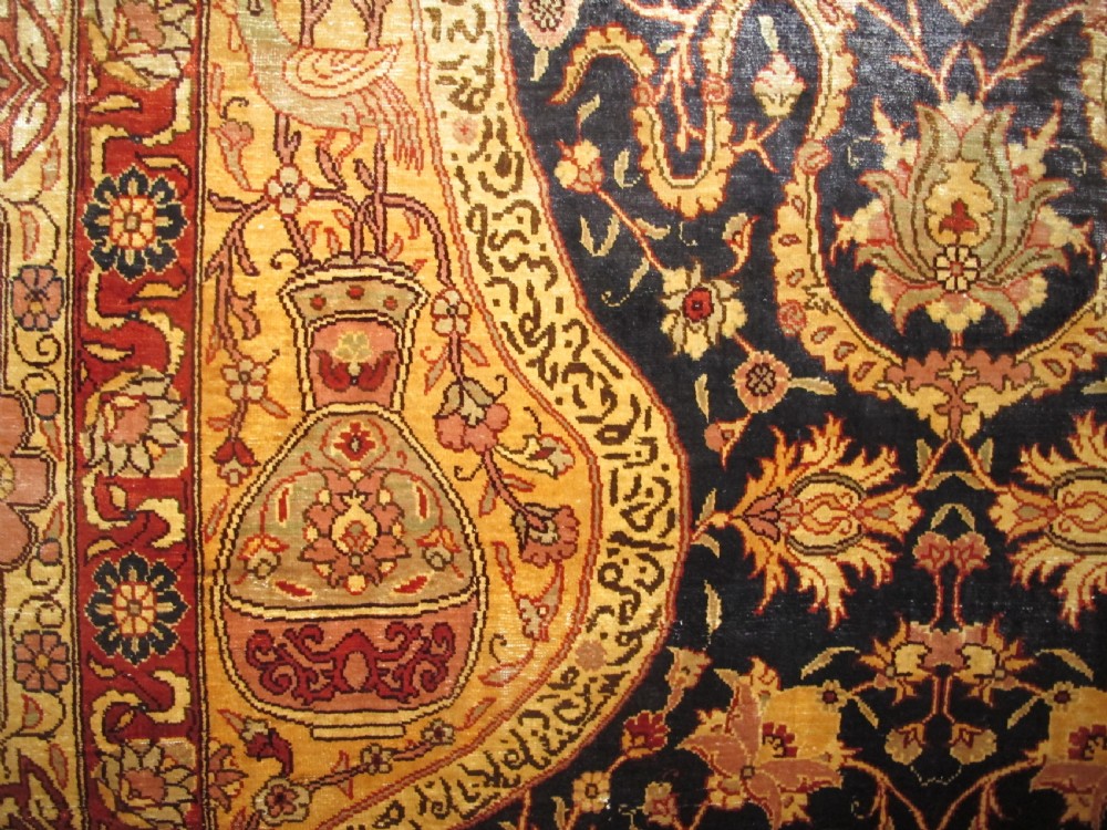 A mid-20th-century Turkish silk rug featuring a dark navy mihrab arch filled with floral motifs, surrounded by an ochre border with calligraphic script and bird illustrations. View VII