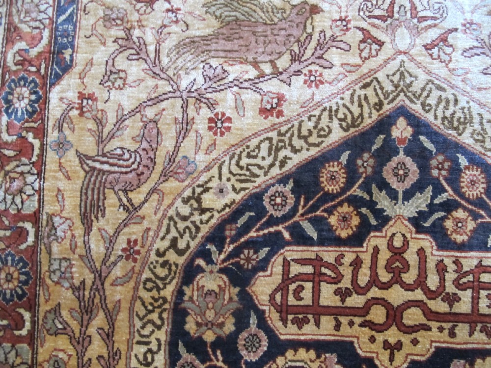 A mid-20th-century Turkish silk rug featuring a dark navy mihrab arch filled with floral motifs, surrounded by an ochre border with calligraphic script and bird illustrations. View X